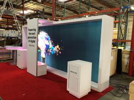 RENTAL: Modified RE-2119 Inline Design with White Laminated Backwall with Lightbox, (2) White Laminated Workstations with Locking Doors, White Laminated Storage Box, Gravitee Arch Canopy, RE-704 Charging Station Table, SEG Fabric Graphics, and Vinyl Appli